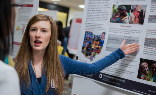 Young woman pointing to her research poster at conference