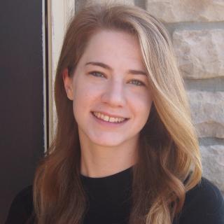 Portrait of Emma Rademacher wearing short sleeve black shirt with stone wall in background